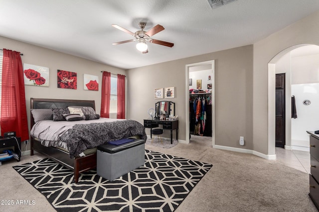 bedroom featuring light carpet, visible vents, arched walkways, baseboards, and a walk in closet