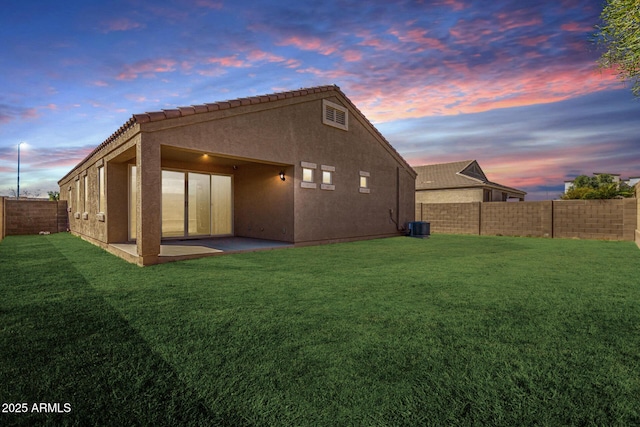 back of house at dusk featuring a lawn, a patio area, a fenced backyard, and stucco siding