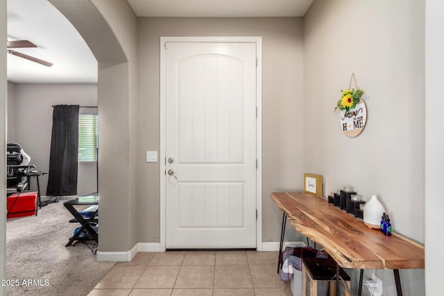 entryway with a ceiling fan, arched walkways, baseboards, and light tile patterned floors