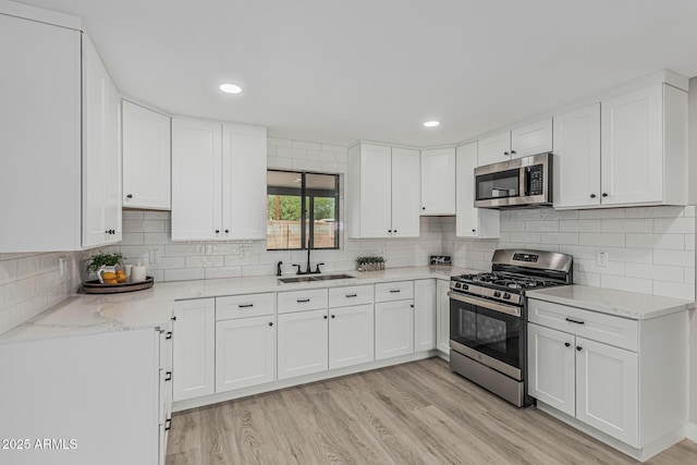4441 N 27th Dr, Phoenix, AZ 85017 - kitchen featuring stainless steel appliances, a sink, light wood finished floors, white cabinetry, and decorative backsplash