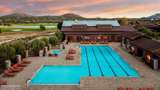 pool at dusk featuring a mountain view, a jacuzzi, and a patio area