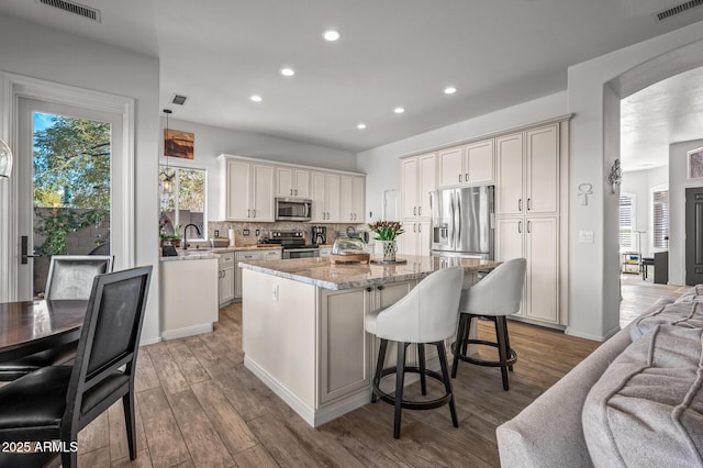 kitchen featuring decorative backsplash, hanging light fixtures, a center island, stainless steel appliances, and light stone countertops