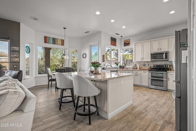 kitchen with decorative light fixtures, a center island, appliances with stainless steel finishes, white cabinets, and backsplash