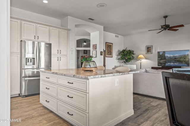 kitchen featuring stainless steel fridge, ceiling fan, a center island, light stone counters, and light hardwood / wood-style floors