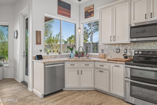 kitchen with sink, appliances with stainless steel finishes, hanging light fixtures, plenty of natural light, and light wood-type flooring