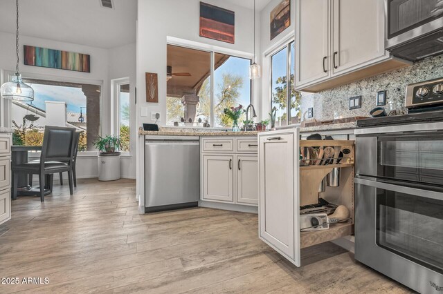 kitchen featuring appliances with stainless steel finishes, tasteful backsplash, light hardwood / wood-style floors, white cabinets, and decorative light fixtures