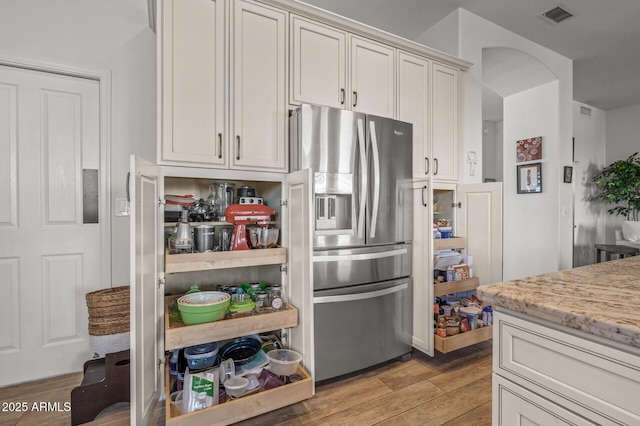 kitchen featuring stainless steel fridge with ice dispenser, light hardwood / wood-style floors, and light stone countertops