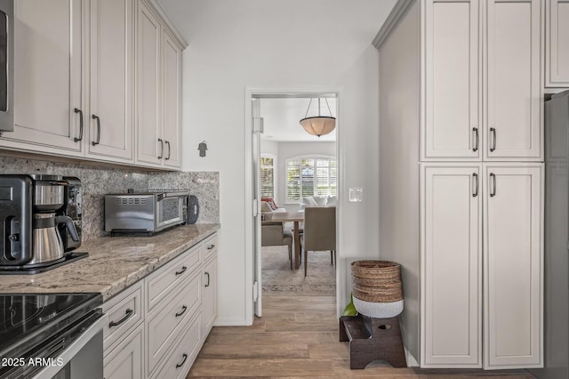 kitchen with white cabinetry, light stone counters, backsplash, and light wood-type flooring