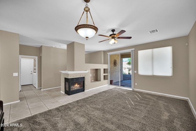 unfurnished living room with a tiled fireplace, light colored carpet, and ceiling fan