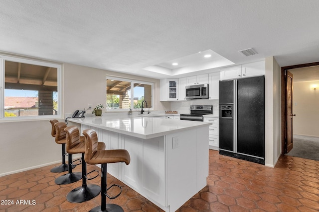 kitchen featuring white cabinets, a textured ceiling, appliances with stainless steel finishes, and a kitchen bar