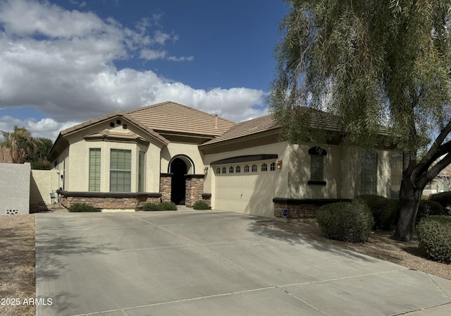 view of front of home with concrete driveway, a tile roof, stucco siding, a garage, and stone siding