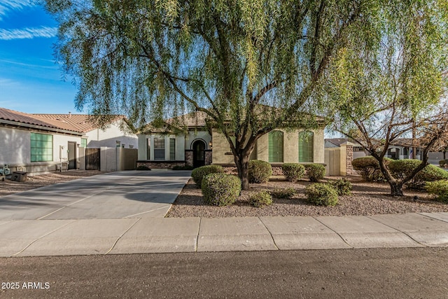 view of front of home with stucco siding, a gate, stone siding, fence, and concrete driveway