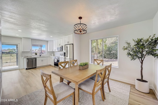 dining room with a wealth of natural light, light hardwood / wood-style floors, a textured ceiling, and a notable chandelier