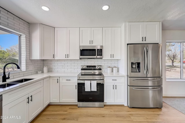 kitchen featuring sink, light wood-type flooring, a textured ceiling, white cabinetry, and stainless steel appliances