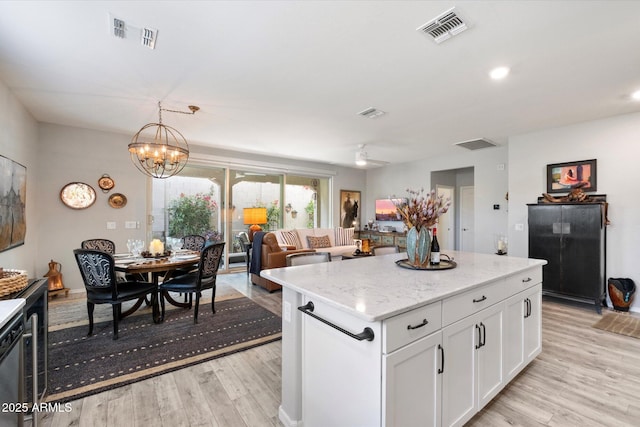 kitchen with light stone counters, white cabinets, decorative light fixtures, light hardwood / wood-style floors, and a kitchen island