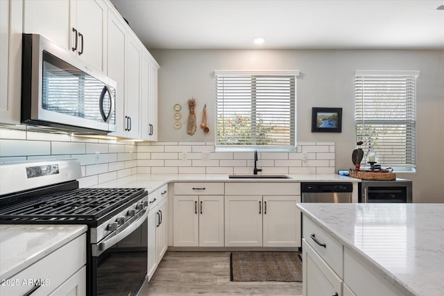 kitchen with appliances with stainless steel finishes, tasteful backsplash, light stone countertops, white cabinets, and sink