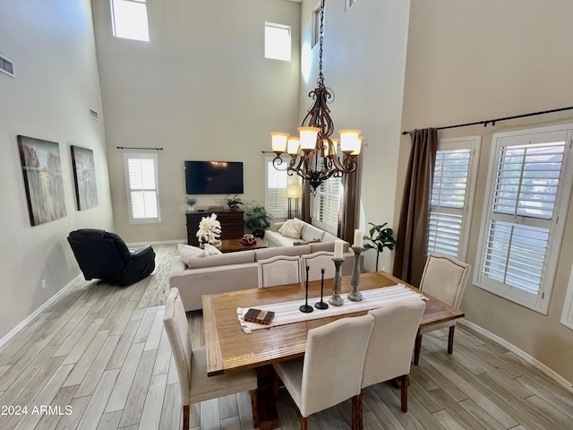 dining space with a healthy amount of sunlight, a towering ceiling, light hardwood / wood-style flooring, and a notable chandelier