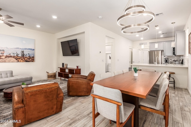 dining space with ceiling fan with notable chandelier and light hardwood / wood-style flooring