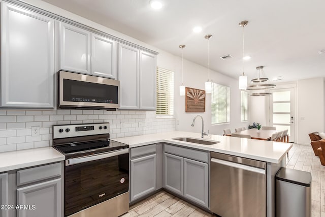 kitchen featuring sink, gray cabinetry, decorative light fixtures, appliances with stainless steel finishes, and light wood-type flooring