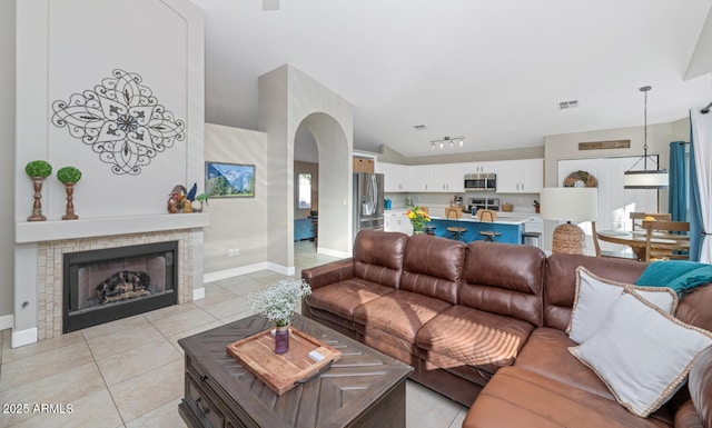 living room with visible vents, arched walkways, a tiled fireplace, track lighting, and light tile patterned flooring