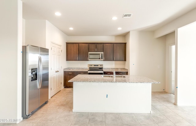 kitchen with a center island with sink, visible vents, appliances with stainless steel finishes, dark brown cabinets, and a sink