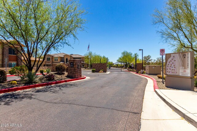 view of asphalt street with curbs, a gated entry, street lighting, a residential view, and a gate