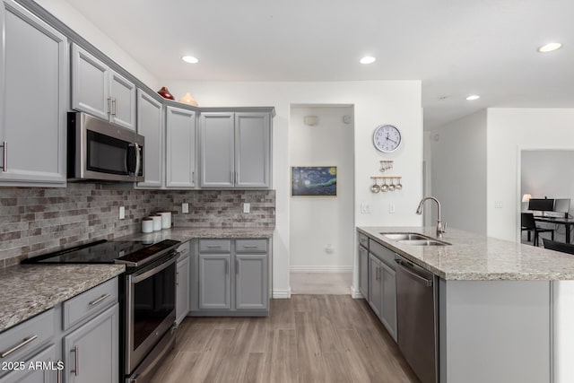 kitchen with appliances with stainless steel finishes, a sink, gray cabinetry, light wood-style flooring, and tasteful backsplash