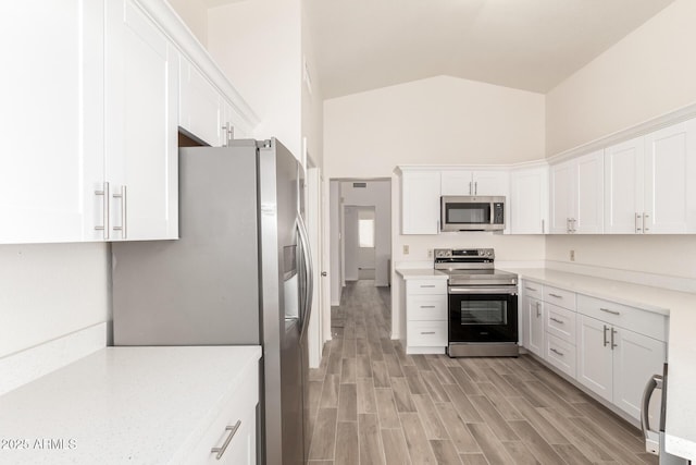 kitchen with light hardwood / wood-style floors, white cabinets, appliances with stainless steel finishes, and high vaulted ceiling