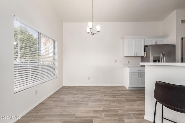 kitchen featuring white cabinetry, light hardwood / wood-style floors, stainless steel refrigerator with ice dispenser, a notable chandelier, and hanging light fixtures