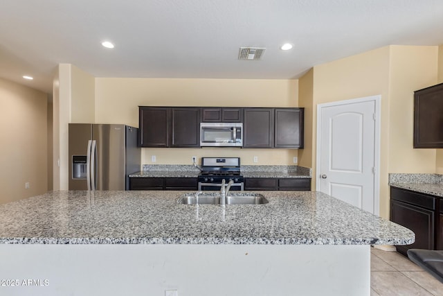 kitchen featuring a sink, visible vents, appliances with stainless steel finishes, light stone countertops, and a center island with sink