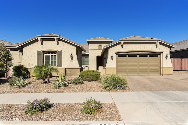 view of front facade with a tile roof, an attached garage, fence, decorative driveway, and stucco siding