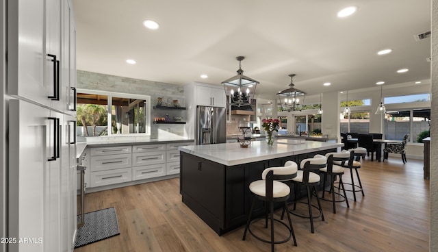 kitchen featuring stainless steel fridge with ice dispenser, a spacious island, decorative light fixtures, light wood-type flooring, and white cabinets