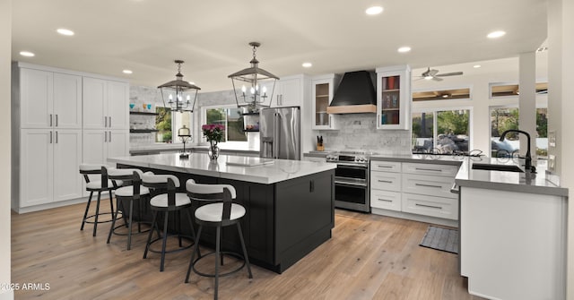 kitchen featuring stainless steel appliances, a breakfast bar, a sink, a center island, and wall chimney exhaust hood