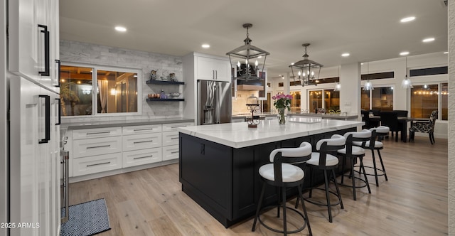 kitchen with light wood-style flooring, light stone countertops, stainless steel refrigerator with ice dispenser, white cabinetry, and open shelves