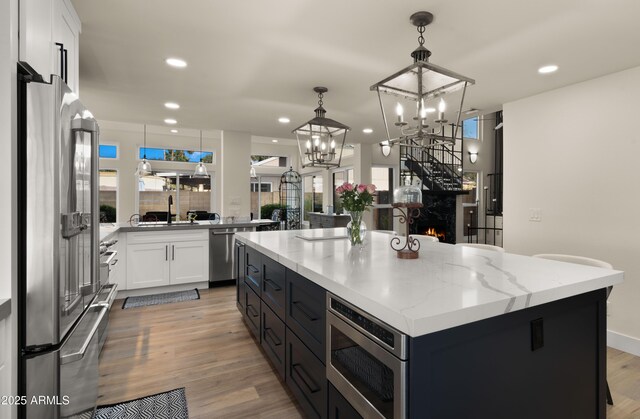 kitchen featuring light stone countertops, stainless steel appliances, light wood-style floors, white cabinets, and a center island