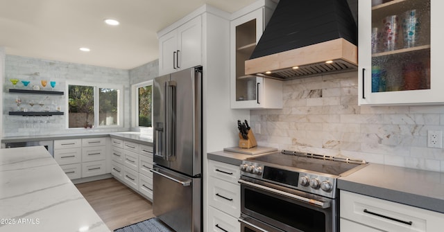 kitchen featuring white cabinets, appliances with stainless steel finishes, light stone countertops, light wood-type flooring, and wall chimney range hood