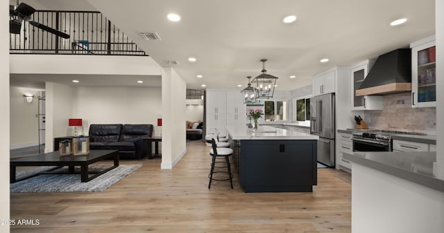 kitchen featuring stainless steel appliances, wall chimney range hood, light wood-type flooring, and visible vents