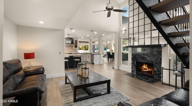 living room featuring baseboards, a high end fireplace, light wood-style flooring, ceiling fan, and recessed lighting