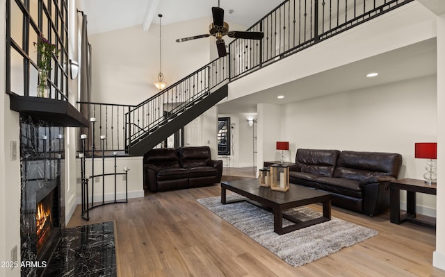 living area featuring a high ceiling, a premium fireplace, wood finished floors, baseboards, and stairs