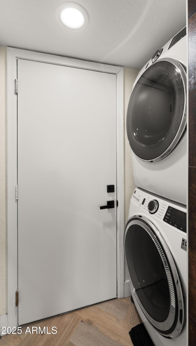 laundry area with a textured ceiling, wood finished floors, and stacked washer / drying machine