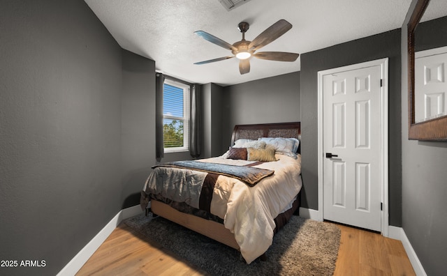 bedroom featuring ceiling fan, a textured ceiling, baseboards, and wood finished floors