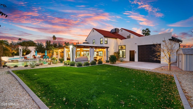 rear view of property with a patio, a garage, fence, a yard, and stucco siding