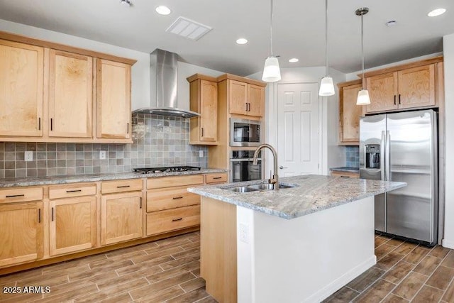 kitchen with wood finish floors, stainless steel appliances, light brown cabinets, a sink, and wall chimney exhaust hood