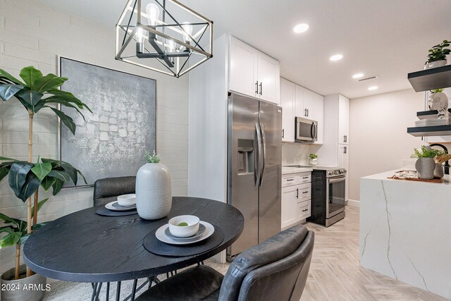 kitchen featuring stainless steel appliances, white cabinets, an inviting chandelier, and light parquet floors