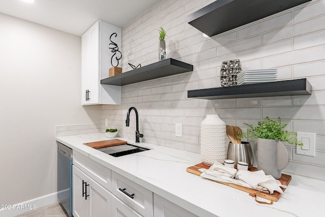 kitchen featuring sink, light stone counters, stainless steel dishwasher, tasteful backsplash, and white cabinetry