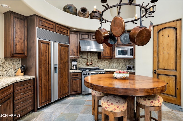 kitchen with dark brown cabinets, built in appliances, light stone counters, and decorative backsplash