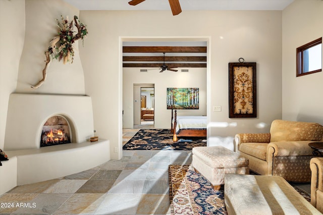 living room featuring ceiling fan, beamed ceiling, and a large fireplace