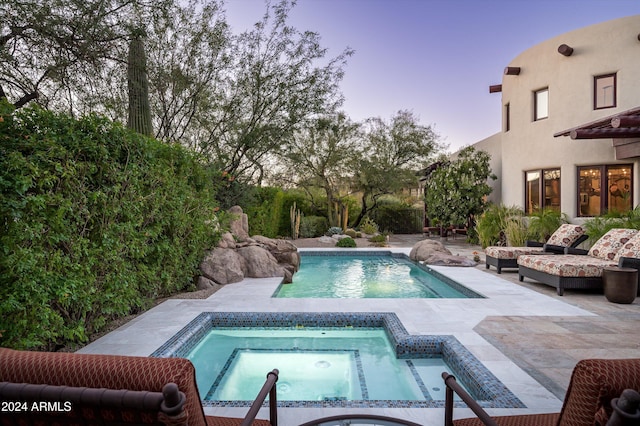 pool at dusk featuring an in ground hot tub and a patio area