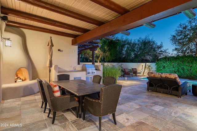 patio terrace at dusk featuring an outdoor kitchen, area for grilling, sink, and an outdoor hangout area