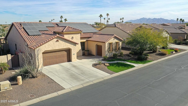 mediterranean / spanish home with stucco siding, driveway, a tile roof, a garage, and solar panels